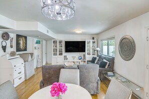 A modern living room with a flat-screen TV, grey sofas, a white coffee table with a vase of flowers, and a chandelier.