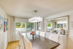 A dining area with a long table, white chairs, a chandelier, and artwork on the walls.