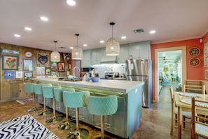 Una cocina con barra, taburetes de bar, una mesa de comedor con sillas y un refrigerador.