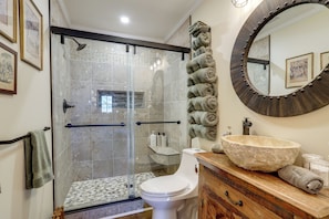 Un baño con ducha de vidrio, inodoro, lavabo con lavamanos de piedra y espejo con marco decorativo.
