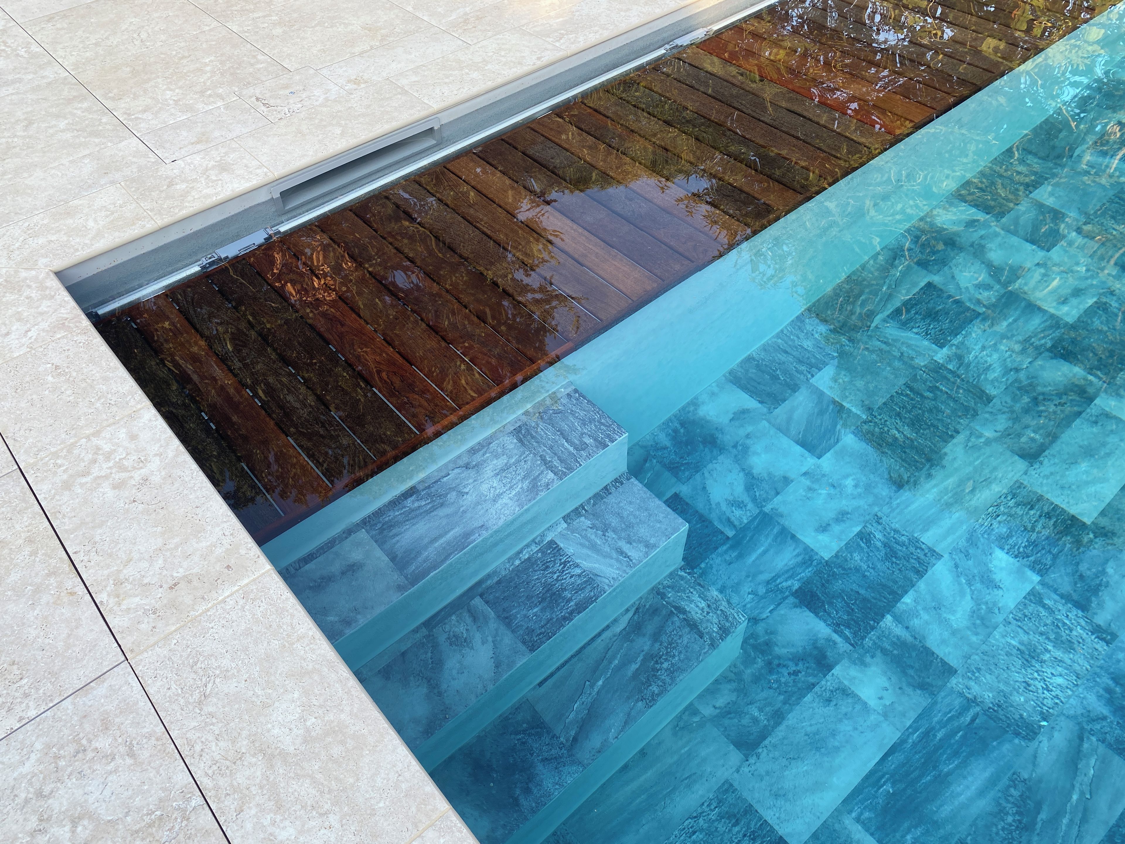 Una piscina con agua cristalina, cubierta de madera y suelo de baldosas.