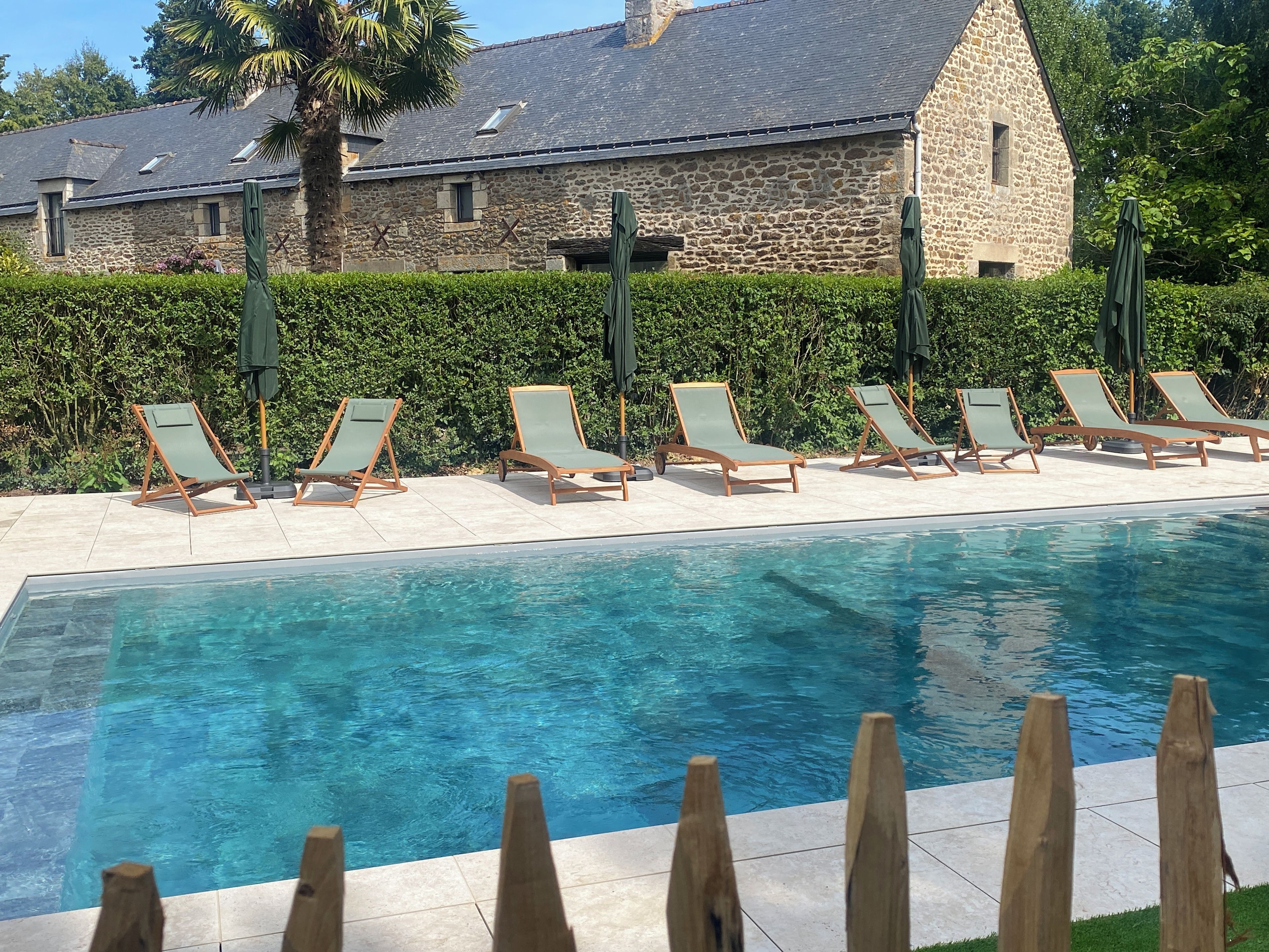 A swimming pool with lounge chairs and a stone building in the background.