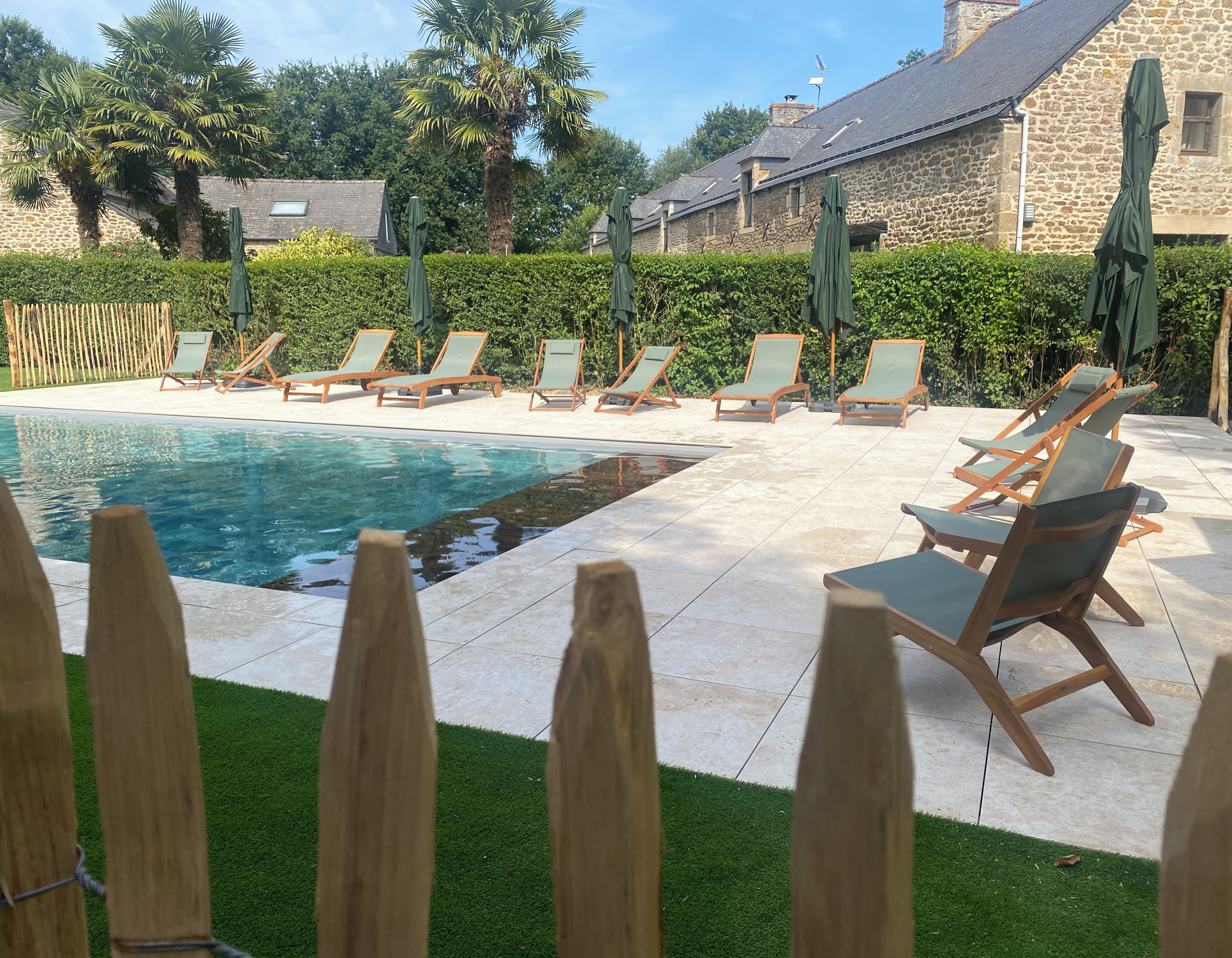 Un área de piscina con sillones de descanso y sombrillas, rodeada de muros de piedra y follaje.