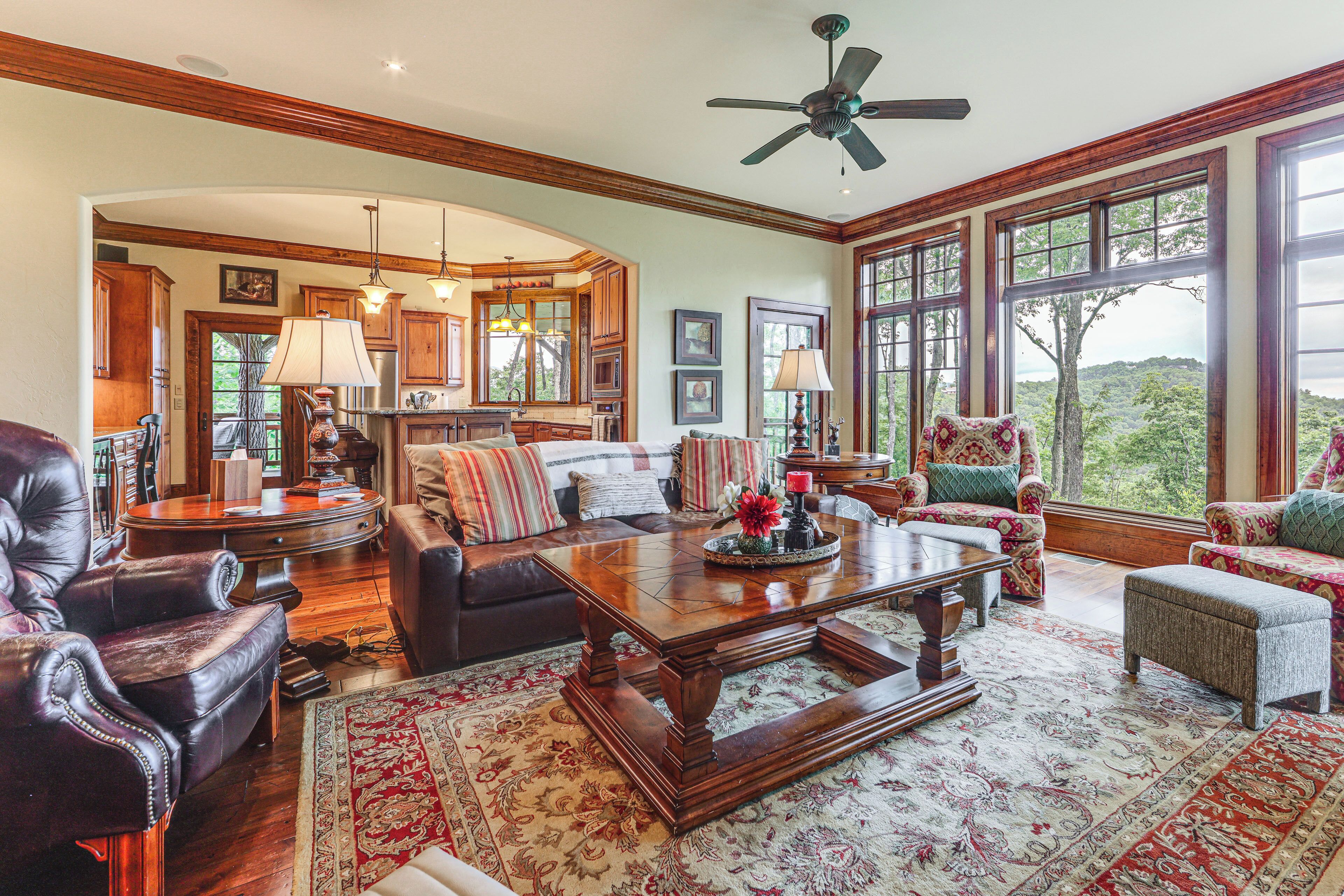A spacious living room with a large wooden coffee table, leather armchairs, and a view of the outdoors through large windows.