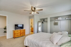 Ein Schlafzimmer mit einem Bett, einem Fernseher, einer Holzkommode, einem Deckenventilator und einem begehbaren Kleiderschrank.
