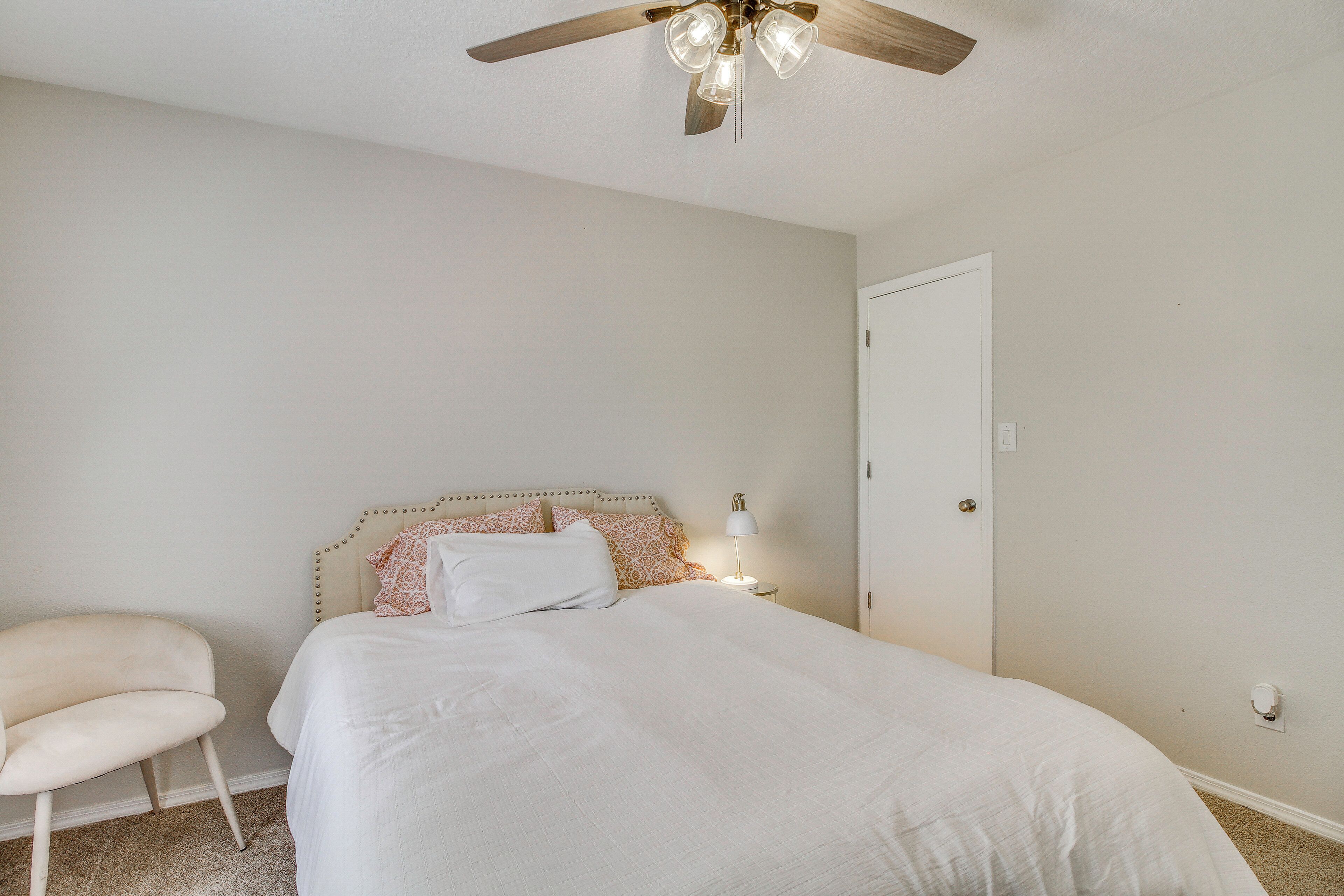 A bedroom with a bed, a chair, a ceiling fan, and a nightstand with a lamp.