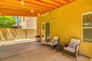 A covered patio area with wicker furniture, a sliding glass door, and a brick wall. - Walkable Home w/ Dog-Friendly Yard in Albuquerque! (Albuquerque)