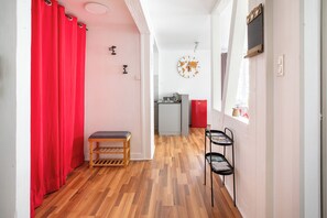 A hallway with a wooden floor, a red curtain, a small bench, a black metal shelf, a gray refrigerator, and a world map on the wall. - Apartment Petite Venise historic center (Colmar)