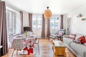 A modern living room with a dining area, large windows, and a sofa with decorative pillows. - Apartment Petite Venise historic center (Colmar)