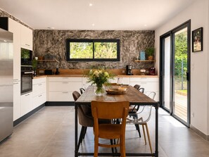 A modern kitchen with a large window, white cabinets, and a dining table with chairs. - Contemporary house with jacuzzi & outdoor space (Les Sables-d´Olonne)