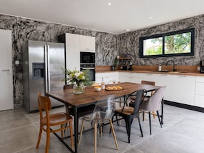A modern kitchen with a marble backsplash, stainless steel appliances, a wooden dining table, and a large window. - Contemporary house with jacuzzi & outdoor space (Les Sables-d´Olonne)