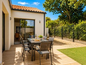 A patio with a table set for dining, a kitchen visible through an open door, and a fenced garden area. - Contemporary house with jacuzzi & outdoor space (Les Sables-d´Olonne)