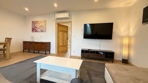 A living room with a white table, a sofa, a TV, a wooden cabinet, and a door.