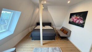 A bedroom with a bed, a sofa, a painting, and a window.