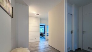 Un pasillo con un banco cubierto de piel, una zona de comedor con una mesa y sillas, y una puerta con rejilla.