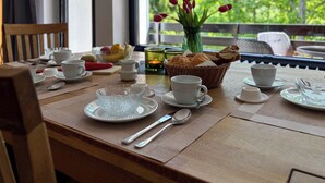 Una mesa de desayuno dispuesta con tazas, platos y cubiertos blancos, una cesta de pan y un jarrón con tulipanes rojos.