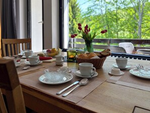 Ein Frühstückstisch reich gedeckt mit weißen Tassen, Tellern und Besteck, einem Brotkorb und einer Vase mit roten Tulpen.