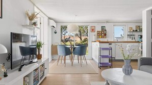 Eine moderne Küche mit weißen Schränken, ein Essbereich mit blauen Stühlen und ein Fernseher links.