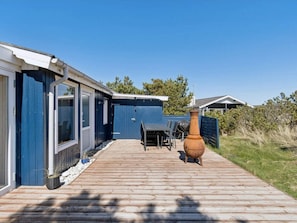 A wooden deck leading to a blue building with a table and chairs, a large pot, and a fence. - 4 Star Holiday Home in Thisted (Thisted)
