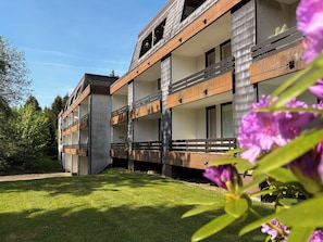 A multi-story building with balconies, a grassy lawn, and a clear sky. - Modern, cozy apartment with pool, right next to the ski slope and golf course in Winterberg (Winterberg)