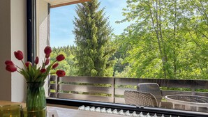 Ein Balkon mit Blick auf Bäume, ein Tisch mit Obstschale und eine Vase mit Blumen.