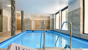 Ein Hallenbad mit großen Glaswänden, Metallleiter und Fliesenboden.