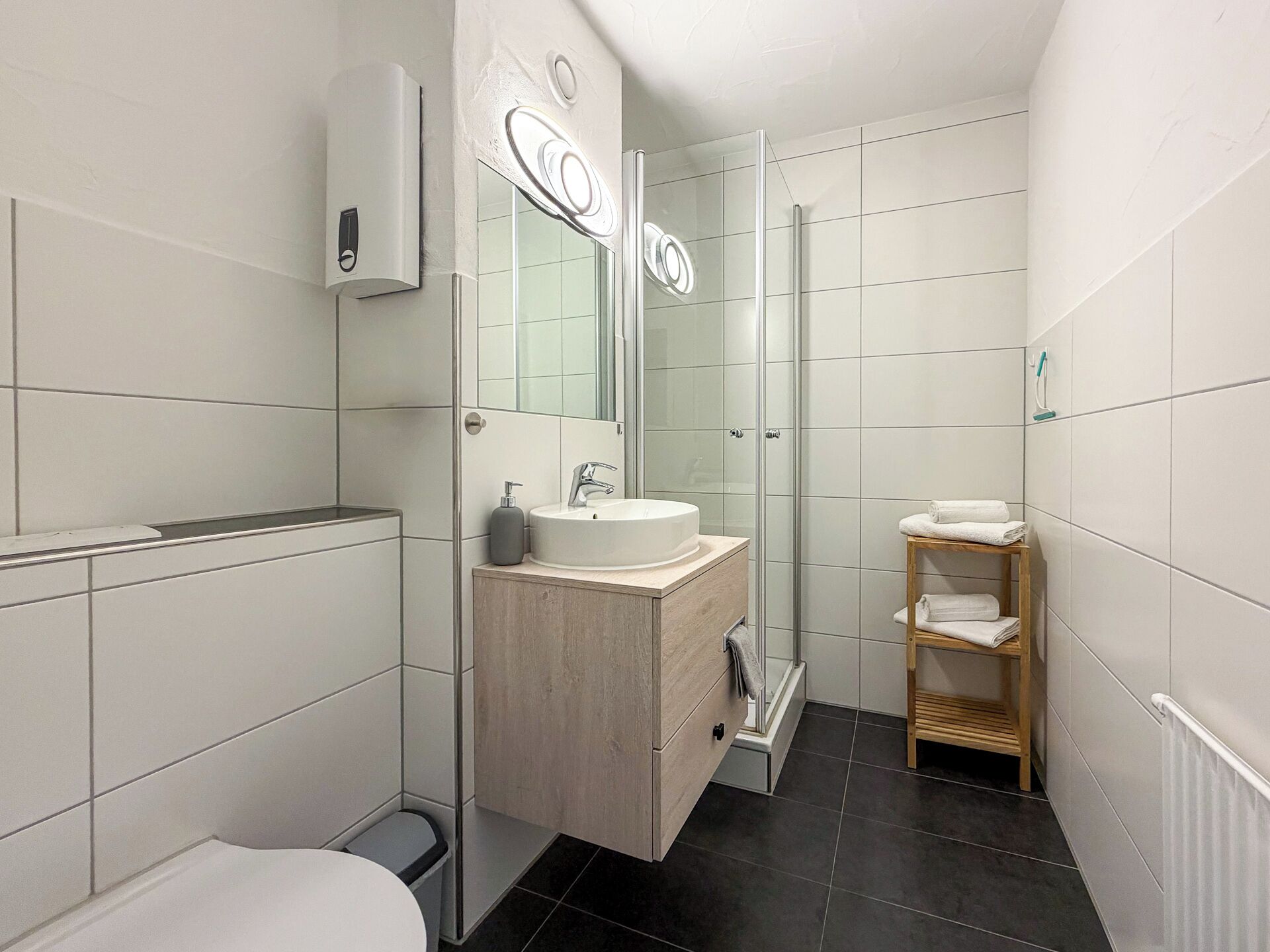 A modern bathroom with a glass shower enclosure, a white sink with a wooden vanity, and a towel rack.