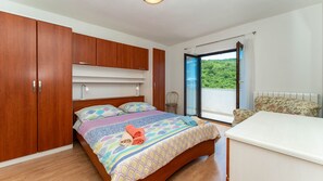 Ein Schlafzimmer mit Bett, Holzschrank, Stuhl, kleinem Tisch und einem Balkon mit Blick.