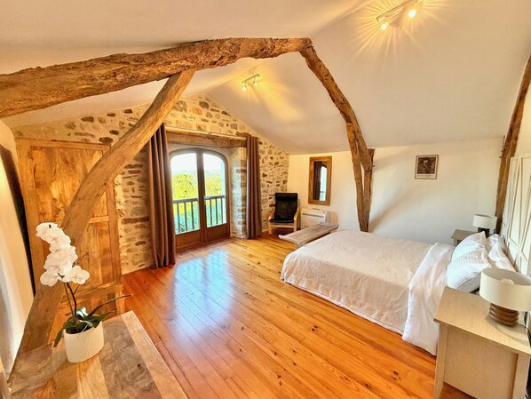 Quarto com teto de madeira, paredes de pedra, uma cama, uma cadeira, uma TV e uma janela com vista.