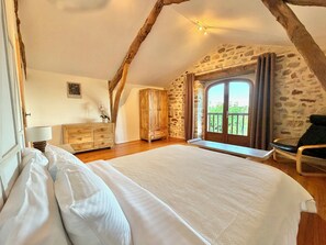 Ein Schlafzimmer mit einem großen Bett, einem Holzschrank, Steinwänden und einem Balkon mit Blick.