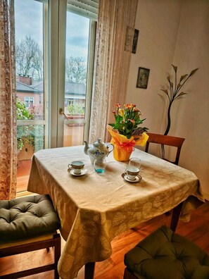 Un coin repas avec une table préparée pour le thé, un vase rempli de fleurs et une vue sur l’extérieur.