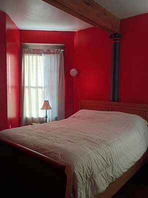 Una habitación con una cama, una ventana con cortinas, una lámpara y una pared roja.