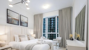 Une chambre d’hôtel moderne avec un grand lit, des tables de chevet, un bureau et une grande fenêtre avec des rideaux.
