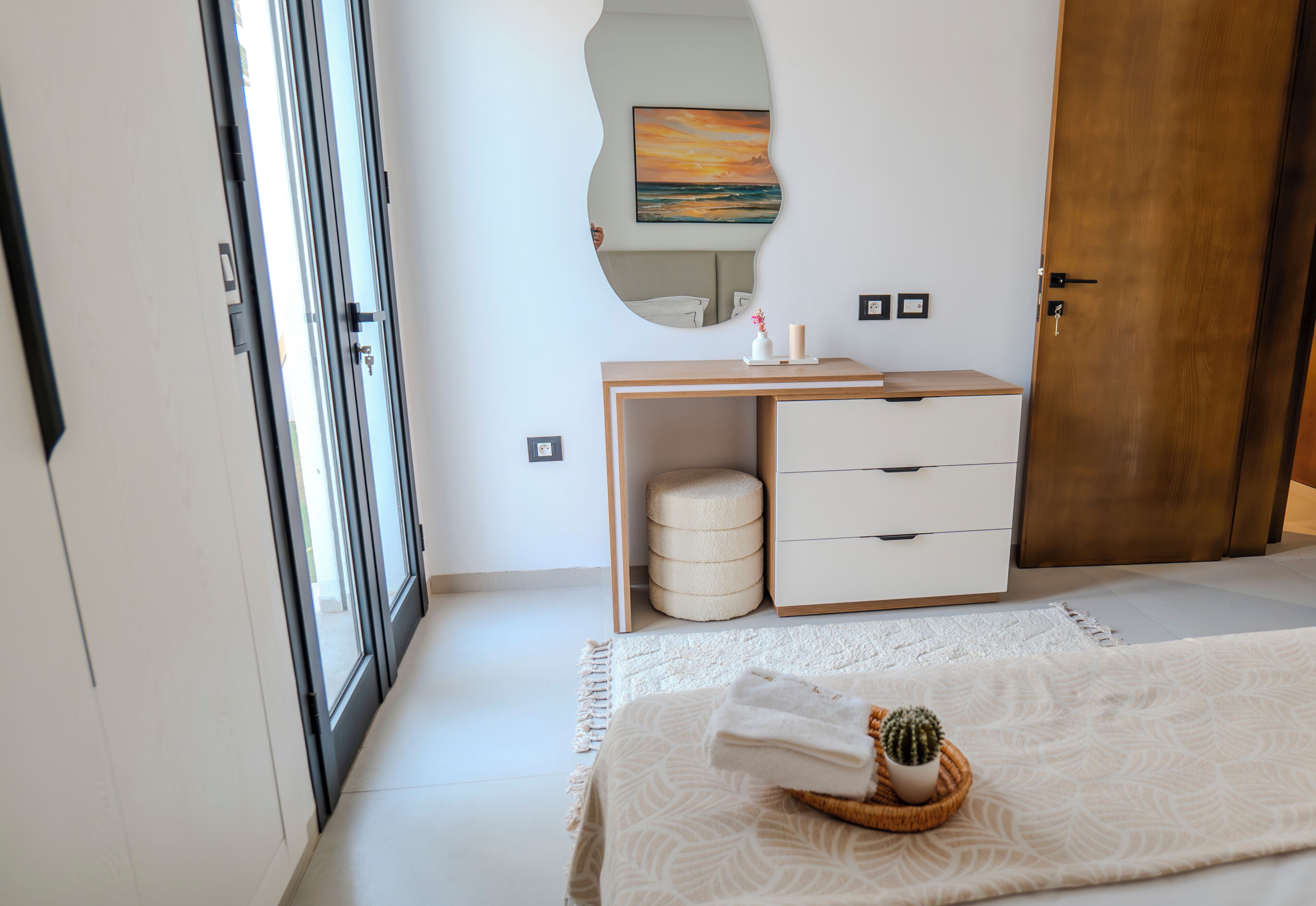 Une chambre à coucher comprenant un lit, une table de chevet, une commode, un miroir et une porte.