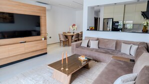 Een moderne woonkamer met een flatscreen televisie, een houten salontafel, een bank en een eethoek met stoelen en een tafel.