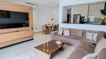 Un salon moderne doté d’un téléviseur à écran plat, d’une table basse en bois, d’un canapé et d’un coin repas avec des chaises et une table.