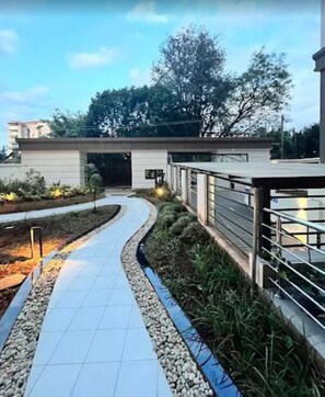 A pathway leading to a building with a modern design, surrounded by greenery and a clear sky. - 108 Riverside View Palace Apartment (Nairobi)