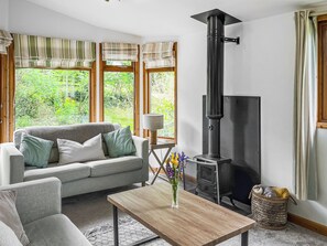 Ein Wohnzimmer mit einer Couch, einem Tisch, einer Lampe, einem Kamin und einem Fenster mit Vorhängen.