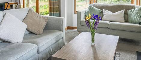 A modern living room with a grey sofa, a wooden coffee table, and a vase with flowers.