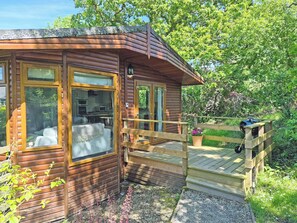 Eine Holzhütte mit großen Fenstern, einer Holzterrasse und einem kleinen Garten.