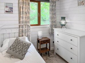 Un dormitorio con cama, mesita de noche, lámpara, cómoda y ventana con cortinas.