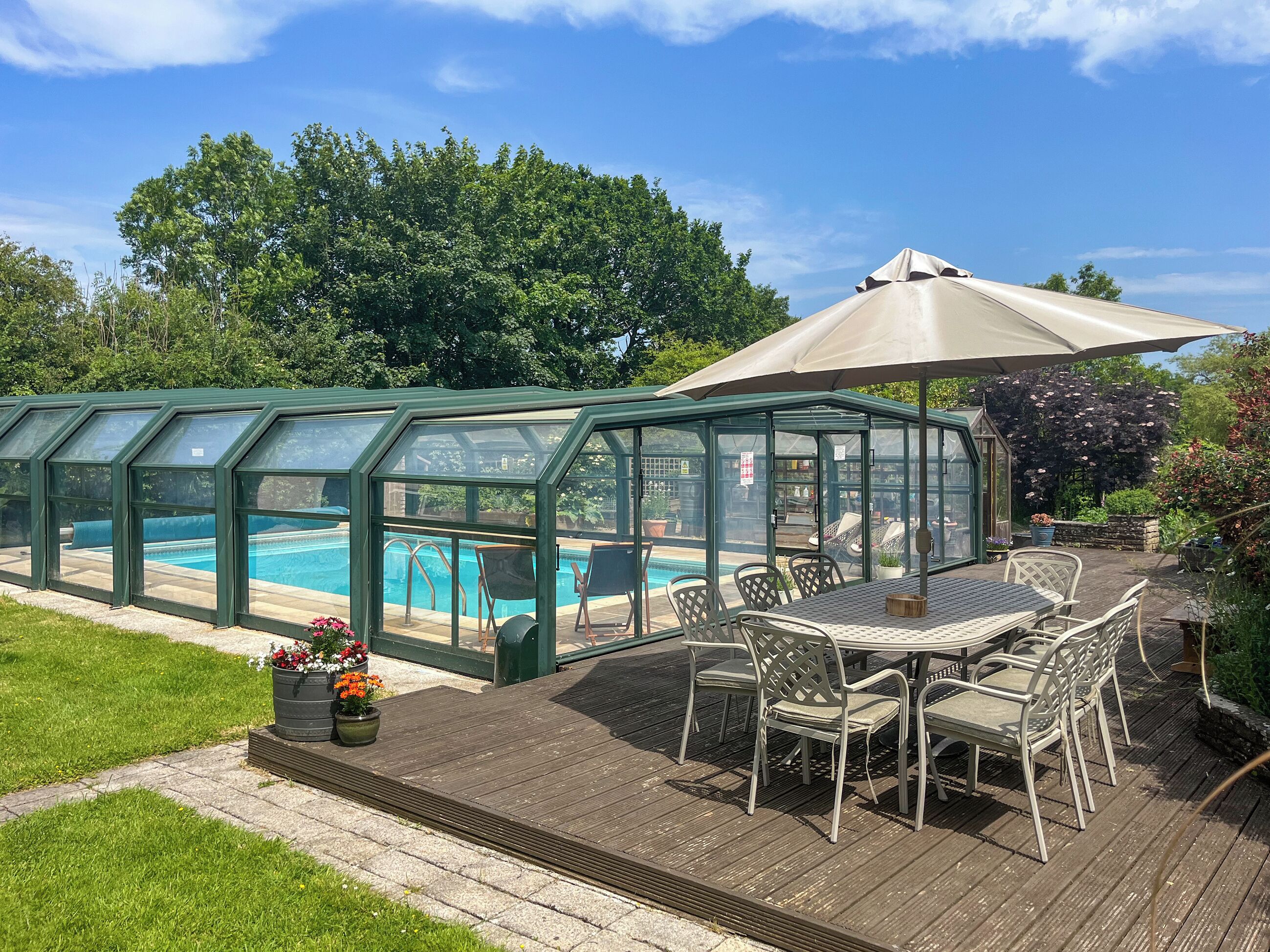 A glass-enclosed pool with a patio area, outdoor furniture, and a large umbrella.