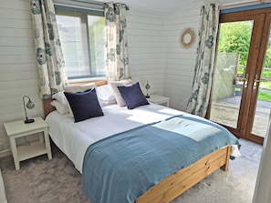 Ein Schlafzimmer mit Bett, Nachttisch, Lampe und Blick ins Freie.