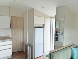 Eine kleine Küche mit einem K ühlschrank, einem Mülleimer und einer Holztür.