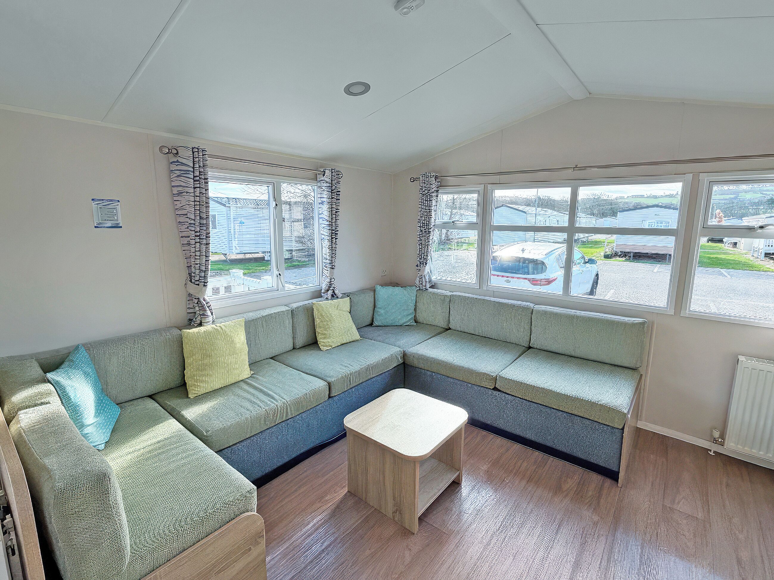 A room with a sectional sofa, a small wooden table, and large windows with curtains.