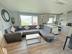 A modern living room with a sectional sofa, a dining table, and a kitchen area with a stove and microwave. - Palm Grove 1 - UKC9556 (Chapel St Leonards)