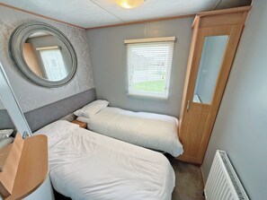 Ein kleines Zimmer mit zwei Betten, einem Spiegel, einem Fenster mit Jalousien und einer Heizung.
