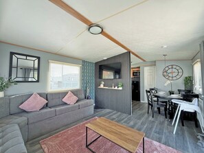 Ein modernes Wohnzimmer mit einem grauen Sofa, einem Holztisch und einem Essbereich mit Tisch für vier Personen.