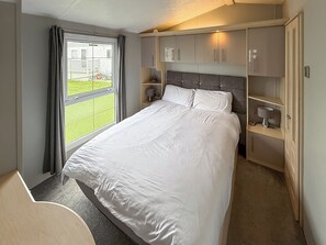 A hotel room with a bed, a desk, a chair, a window with curtains, and built-in cabinets. - Palm Grove 2 - UKC9557 (Chapel St Leonards)