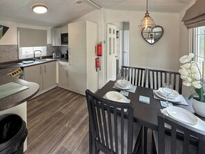 A compact kitchen with a microwave, stove, and sink, a dining area with a table set for four, and a heart-shaped light fixture. - Palm Grove 2 - UKC9557 (Chapel St Leonards)